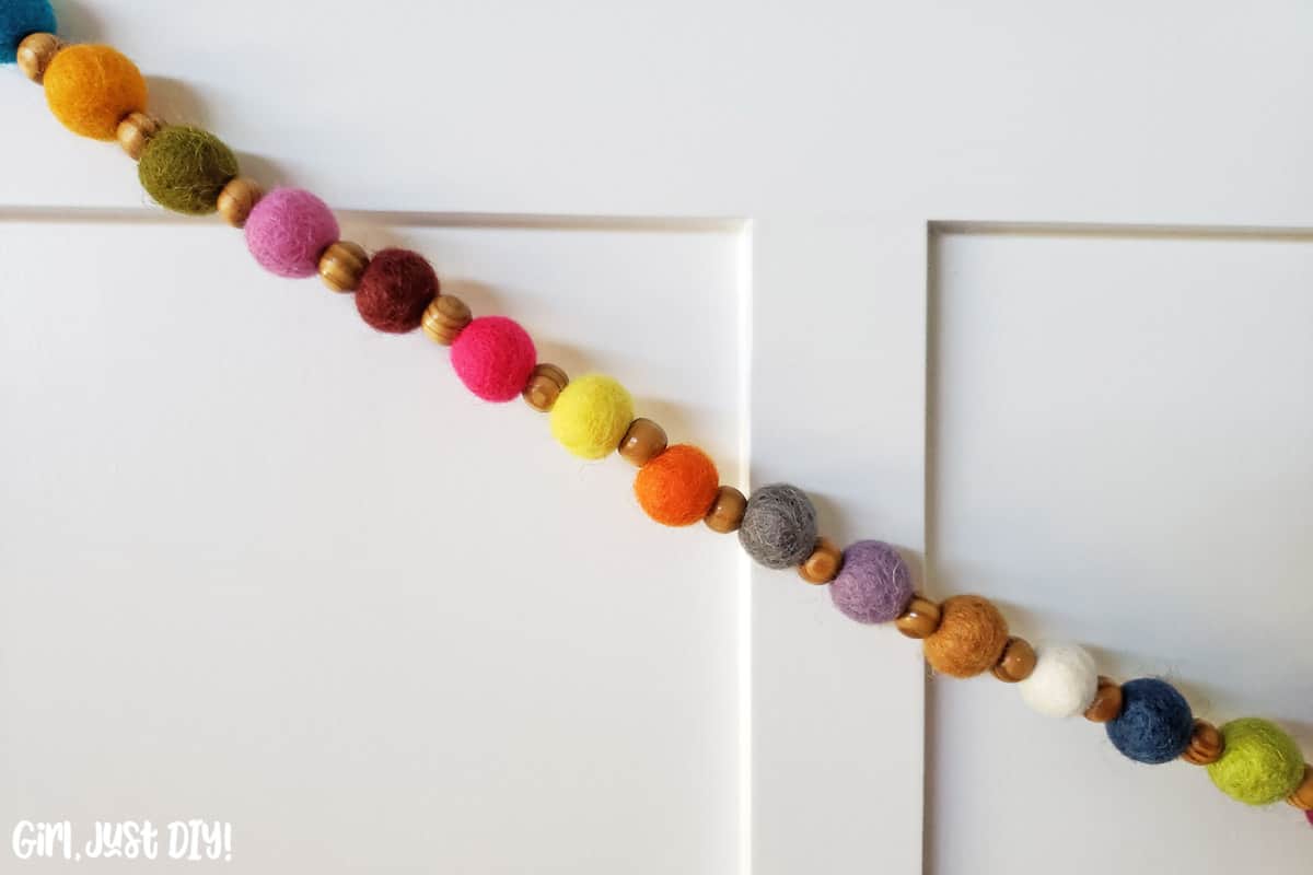 closeup of felt ball garland hanging on face of white cabinet face.
