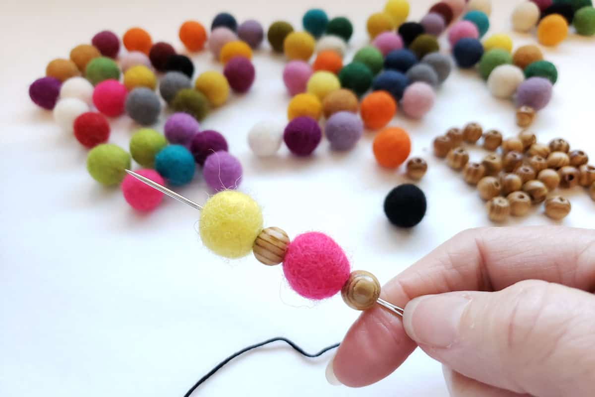 felt balls and wood beads threaded onto long needle with colorful felt balls iin background