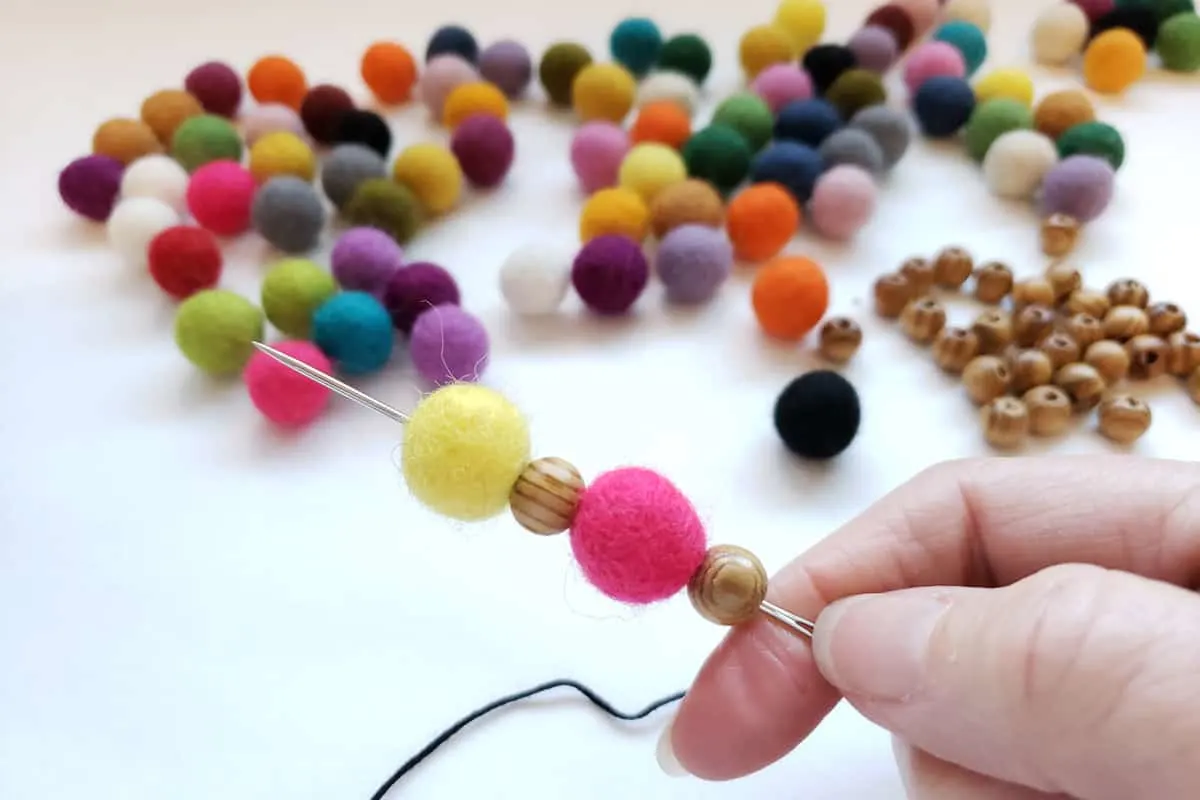 felt balls and wood beads threaded onto long needle with colorful felt balls iin background