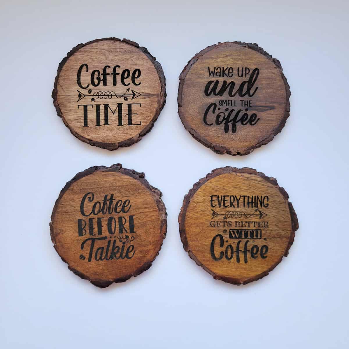 Four completed engraved wood coasters with various sayings about coffee.