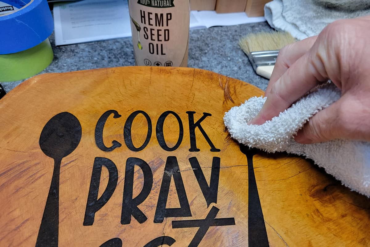 Rubbing hemp oil with cloth onto engraved cutting board.